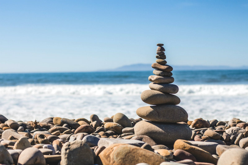 Cairn of 12 pebbles against a seaside background.