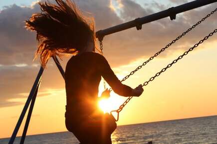 Sun setting behind a young woman on a swing, illustrating the idea of playing with God.