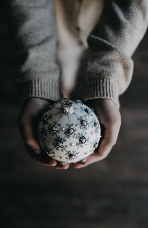 Outstretched hands holding a white bauble, decorated with silver filigree.