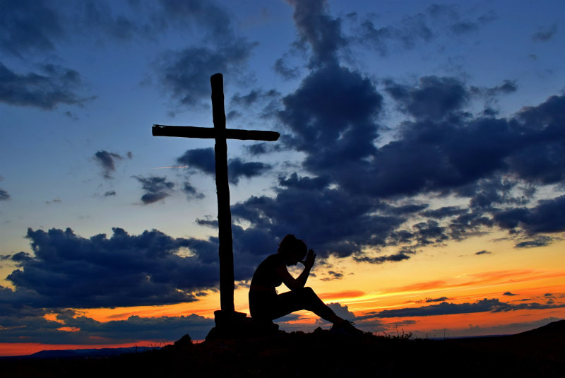 Outline of cross against sunset, with figure thinking.