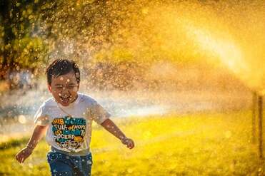 Young child, excitedly running through a glistening water-spray, illustrating the section, ’Be Like Little Children’.