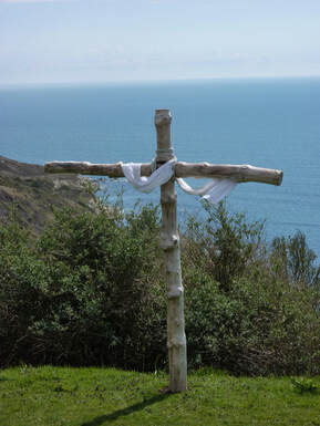 Cliff-top cross with blowing white mantle, looking out to sea, illustrating Jesus’ words ‘It is finished’.