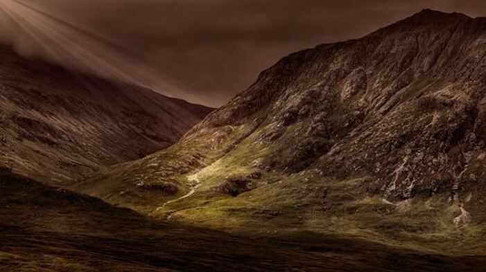 Dark mountainous valley, with light rays focused on one spot.
