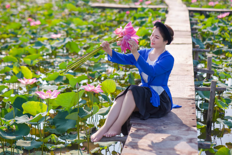 Girl sitting on a wooden walkway through a lily pond, holding a bunch of large-headed bright pink lilies.