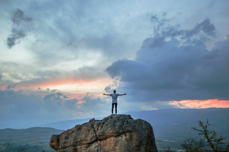 Man on rock with arms outstretched.