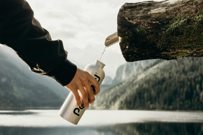 Mountain lake, person apparently filling a water bottle from a spout in a log.