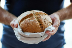 Hands carrying a fresh loaf of bread.