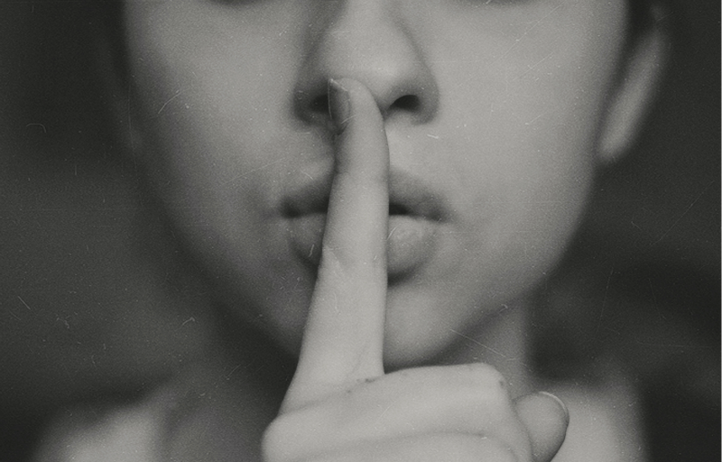 Close-up of woman with finger over her lip signalling quiet.