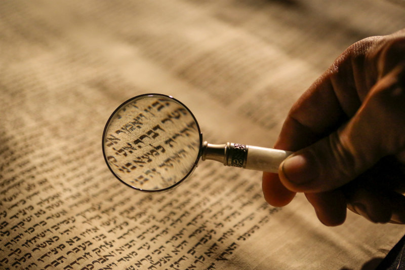 Magnifying glass held over a portion of Hebrew scripture.