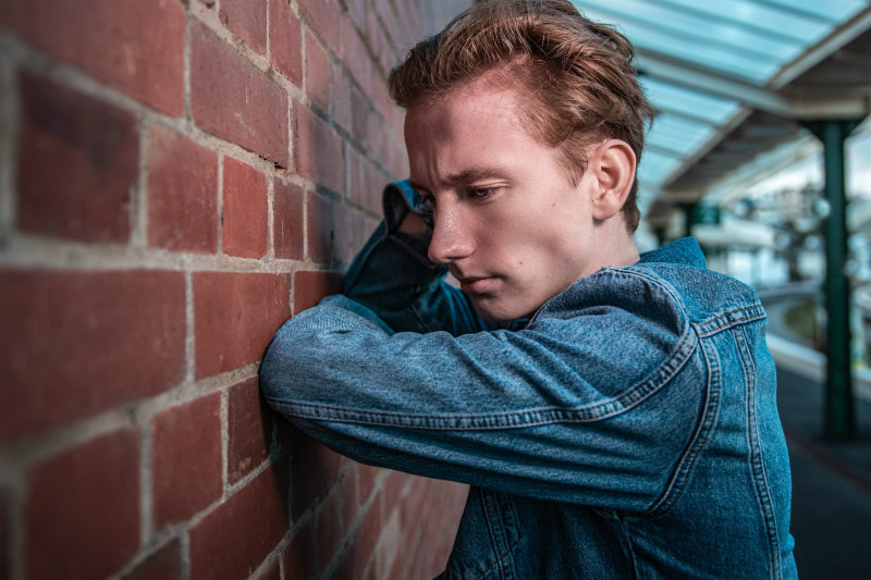 Close-up of frowning man, leaning against a wall.