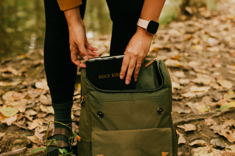 Close-up of a woman's hands putting a Bible in a rucksack.