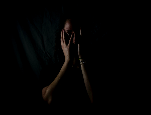Girl sitting in darkness, hands over her face, illustrating blog theme, 'Free from fear'.