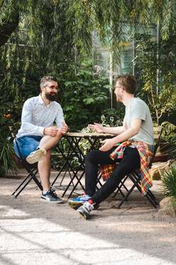 Two younger men chatting in a leafy courtyard, illustrating the idea that the tongue has the power of life and death.