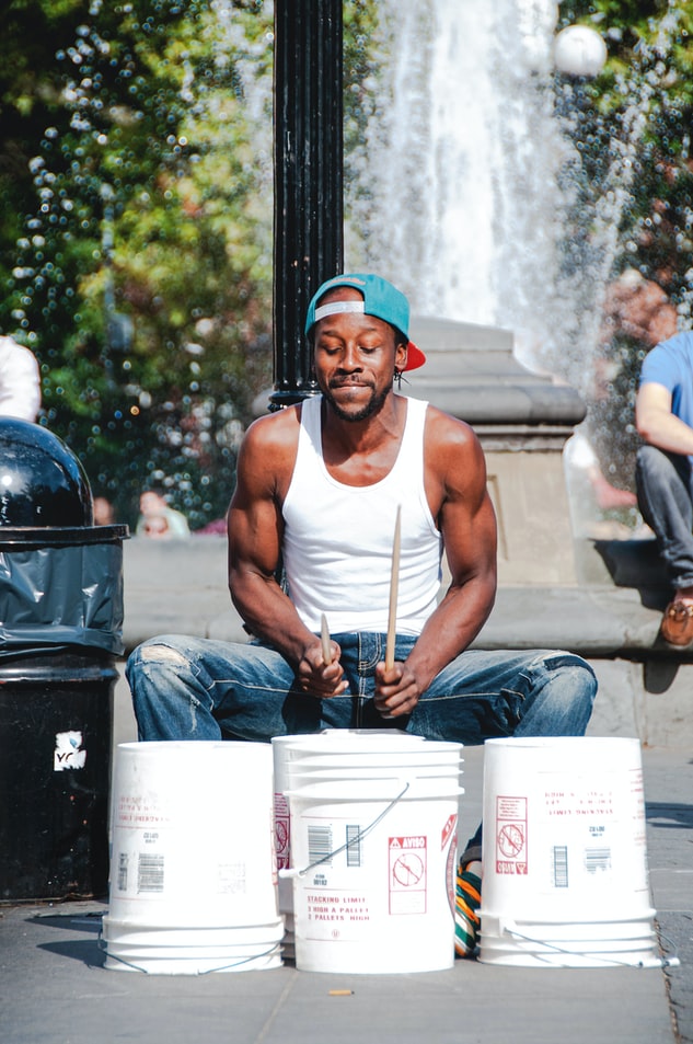 A street-drummer, playing on upturned tubs, by a fountain, illustrating the explanation of ‘rhythms of grace’.